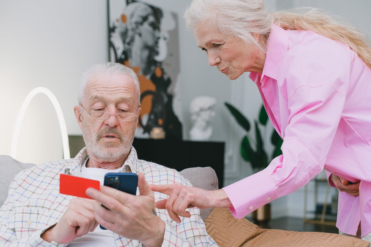 journey Elderly couple handling credit card transaction on smartphone indoors.